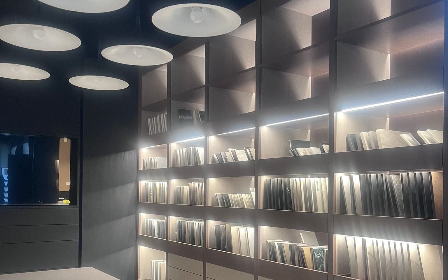 Stół roboczy w showroomie GRES DESIGN z podświetlaną biblioteką wzorników w tle